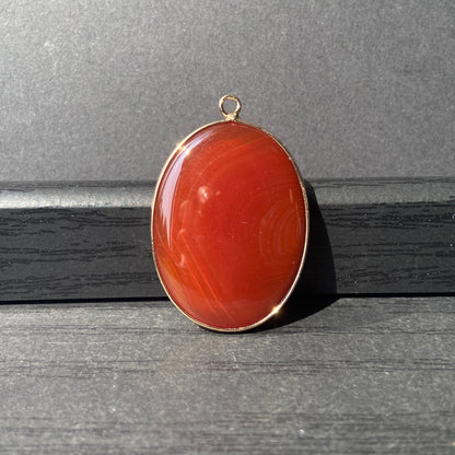 Handgeschliffener ovaler Naturstein Anhänger aus rotem Achat mit goldfarbener Fassung für DIY Schmuckherstellung und Boho Halsketten
