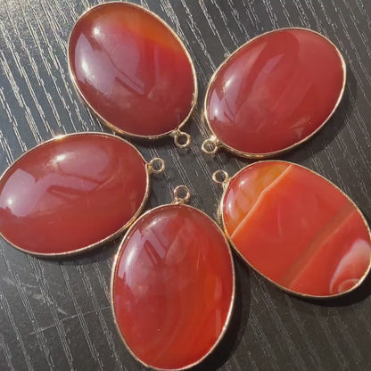 Handgeschliffener ovaler Naturstein Anhänger aus rotem Achat mit goldfarbener Fassung für DIY Schmuckherstellung und Boho Halsketten